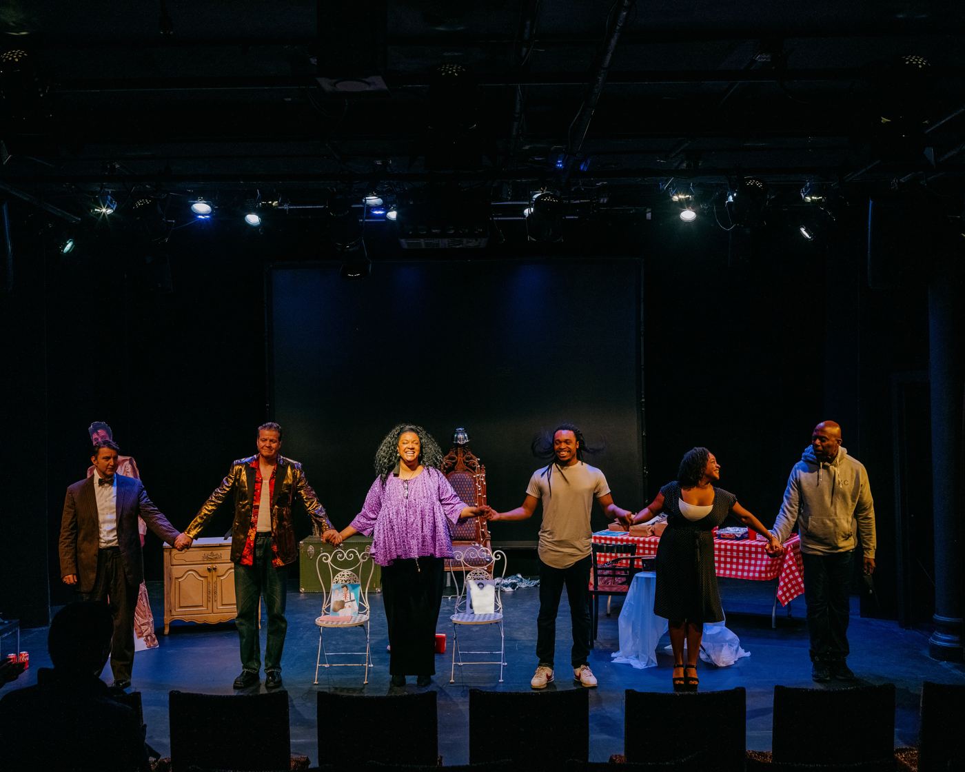 The full company joins hands for a curtain call on the dark stage.
